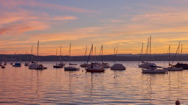 Bodensee Gölü Gündoğumu Panoraması. Sükunet Suları Üzerine Sabah Güneşi. Alman Bodensee Gölü üzerindeki büyüleyici şafağa tanık olun. Bir tekne iskelesinden yakalandılar. İlk zamanların huzurlu güzelliğini kucakla.