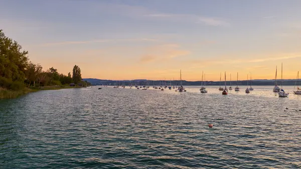 Bodensee Gölü Panorama. Akşam, alacakaranlık, batan güneş, manzara, sakin sular, rıhtımda tekneler ve yatlar, suda yansıyan bulutlar, alacakaranlıkta nehir kenarı.