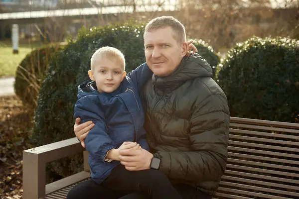 Sonbahar Aile Sevgisi: 40 yaşındaki baba ve Oğul - 8 yaşındaki güzel çocuk, parkta oturuyor. Sonbahar havasındaki aile sevgisinin sıcaklığını bu iç açıcı görüntüyle kucaklayın. Bir baba.