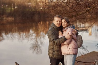 Sevgili çift sonbaharda parkta göletin kıyısında oturur. Bir erkek ve bir kadın. Bir çift, göl kıyısında yürüyen aşıklar.