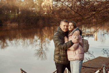 Sevgili çift sonbaharda parkta göletin kıyısında oturur. Bir erkek ve bir kadın. Bir çift, göl kıyısında yürüyen aşıklar.