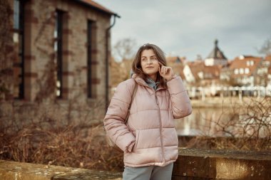 Young beautiful pretty tourist girl in warm hat and coat with backpack walking at cold autumn in Europe city enjoying her travel in Zurich Switzerland. Outdoor portrait of young tourist woman enjoying clipart