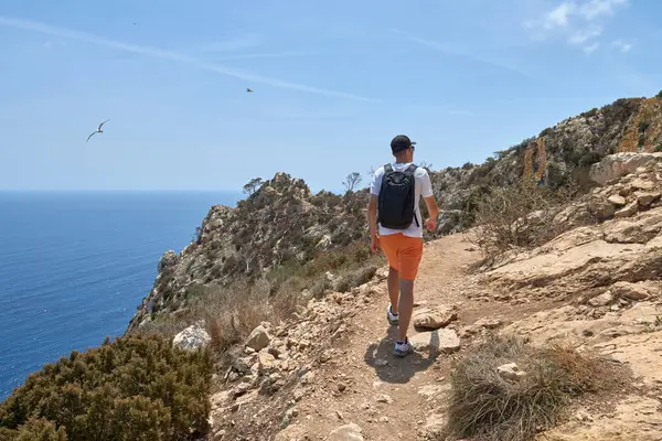 stock image Daring Twenty-Year-Old Explorer Traversing Breathtaking Cliff-Side Path with Panoramic Ocean Views on Sunny Summer Day