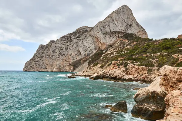 stock image Serene coastal landscape with rocky cliffs and turquoise ocean under bright sunny sky in Calpe Spain perfect for tourism