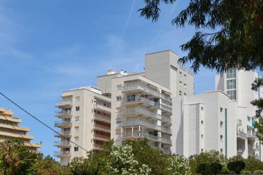 Modern İspanyol Metropolü: Pürüzsüz gökdelenler ve Berrak Yaz Gökyüzü tarafından Çerçevelenmiş Lush Palm Trees. Idyllic Spanish Cityscape: Yüksek Binalı Mimari ve Palmiye Ağaçları Yaz Güneşi 'nin Sıcaklığında Parlıyor