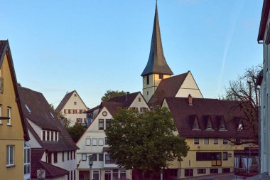 A picturesque view of a historic village featuring a prominent church steeple against a twilight sky. clipart