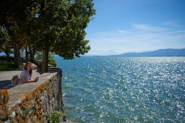 Lindau, Almanya 'daki Ortaçağ Kalesi Duvarları' ndan Bodensee Panorama 'ya hayran olan Büyüleyici Genç Kadın. Idyllic Yaz Sahnesi Alp Dağları, Yat ve Serene Gölü ile Avrupa Tatil Mutluluğunu Yakalıyor