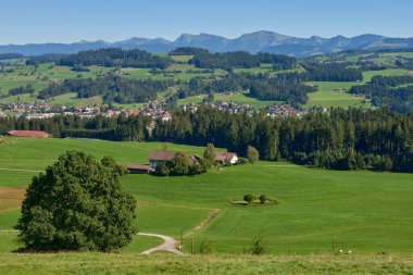 Bu büyüleyici görüntü Alp eteklerindeki kırsal yaşamın dingin güzelliğini gözler önüne seriyor. Geleneksel çiftçi çiftlikleri yemyeşil arazide, kırsal mimarileri uyum içinde harmanlanıyor.