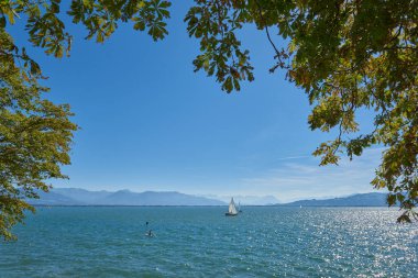 Lindau Showcasing White Yelkenlileri ve İsviçre Alpleri 'ndeki Bodensee' nin Ağaç Kemeri Arasından Görünümü. Idyllic Yaz Günü Avrupa Tatil Cenneti 'ni Denizcilik, Doğa ve Dağ Vistaları ile Ele Geçiriyor