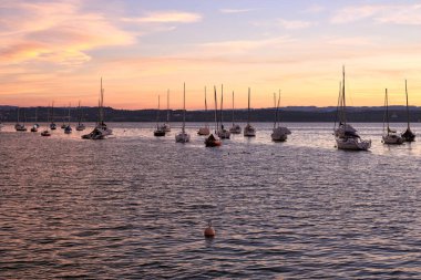 Gün batımının dinginliğini, sakin sulara uzanan bir iskele ve yüzeyde yavaşça sallanan yelkenlilerle dolu bir gölün üzerinde hissedin. Bu sakin rıhtım manzarası,