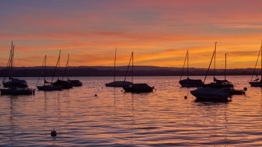 Bodensee Gölü Panorama. Akşam, alacakaranlık, batan güneş, manzara, sakin sular, rıhtımda tekneler ve yatlar, suda yansıyan bulutlar, alacakaranlıkta nehir kenarı.