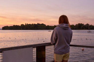 Huzurlu Genç Kadın Nefes Kesen Gündoğumu manzarasının tadını çıkarıyor Tranquil Gölü 'nün yanında Sersemletici Sabah Ufkusu ile. Rastgele Kıyafette Dalgın Kadın Silueti Huzurlu Rıhtım Anı Yakalıyor