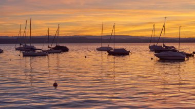 Bodensee Gölü Gündoğumu Panoraması. Sükunet Suları Üzerine Sabah Güneşi. Alman Bodensee Gölü üzerindeki büyüleyici şafağa tanık olun. Bir tekne iskelesinden yakalandılar. İlk zamanların huzurlu güzelliğini kucakla.