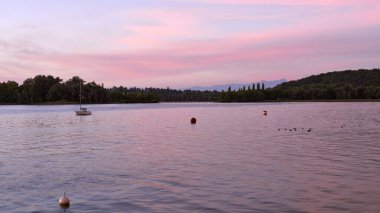 Gün batımının dinginliğini, sakin sulara uzanan bir iskele ve yüzeyde yavaşça sallanan yelkenlilerle dolu bir gölün üzerinde hissedin. Bu sakin rıhtım manzarası,