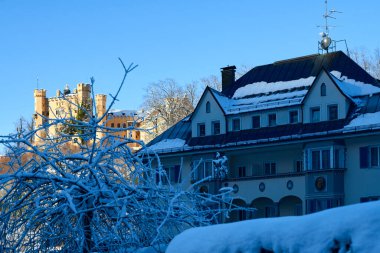 Bu fotoğraf, koyu mavi, karla kaplı çatısı olan çok katlı, büyüleyici bir konut binasının olduğu huzurlu bir kış sahnesini çekiyor. Yumuşak, açık bej rengine boyanmış binanın birkaç tane var.