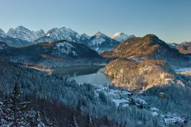 Nefes kesici panoramik manzara Bavyera Alpleri 'ndeki peri masalı kış sahnesinin özünü yakalar. Dünyaca ünlü bir kale, görkemli karlarla kaplı dağlarla çevrili sakin bir göle bakan karla kaplı bir tepenin tepesinde keyif çatıyor. Erken.