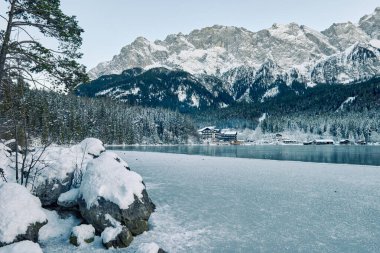 Büyüleyici Alacakaranlık Alp Harikalar Diyarı: Eibsee Gölü Karlı Zugspitze Dağı 'nı Aydınlatılmış Çam Ormanı' nın ortasına yansıtıyor Kış Büyüleyici Manzarası Alman Kayak Resimlerinin Huzurlu Güzelliğini Alacakaranlıkta Yakalıyor. Bu nefes kesici akşam sahnesinde...