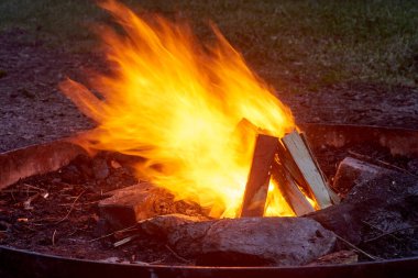 Büyüleyici kamp ateşi sahnesi. Açık havada yanan odunlardan yükselen yoğun turuncu alevleri yakıyor. Fotoğrafları kapat. Güçlü ateş elementleri ve dinamik alev desenleri sergiliyor.