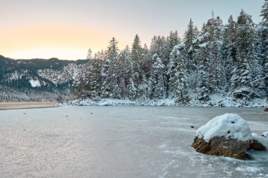 Büyüleyici Alacakaranlık Alp Harikalar Diyarı: Eibsee Gölü Karlı Zugspitze Dağı 'nı Aydınlatılmış Çam Ormanı' nın ortasına yansıtıyor Kış Büyüleyici Manzarası Alman Kayak Resimlerinin Huzurlu Güzelliğini Alacakaranlıkta Yakalıyor. Bu nefes kesici akşam sahnesinde...