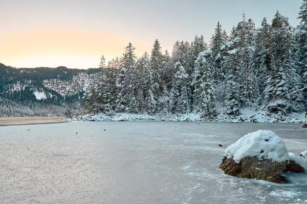 Büyüleyici Alacakaranlık Alp Harikalar Diyarı: Eibsee Gölü Karlı Zugspitze Dağı 'nı Aydınlatılmış Çam Ormanı' nın ortasına yansıtıyor Kış Büyüleyici Manzarası Alman Kayak Resimlerinin Huzurlu Güzelliğini Alacakaranlıkta Yakalıyor. Bu nefes kesici akşam sahnesinde...