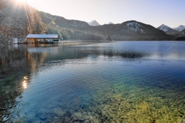Huzurlu Kış Harikalar Diyarı: Donmuş Göl, Altın Sabah Donmuş Dağları Yansıtır. Buz gibi buzlu manzaralar, Kıtır Güneşli bir günde Alp Gölü 'nün nefes kesici güzelliğini yakalar. Bu büyüleyici görüntü, sakin bir kış manzarasını gözler önüne serer.