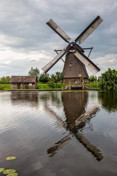 Anaokulundaki bir kanalda rüzgar değirmeni. Yakınlarda suda yansıyan küçük bir ev.