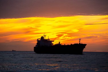 transport ship in front of sunset with clouds and wind turbines at the horizon