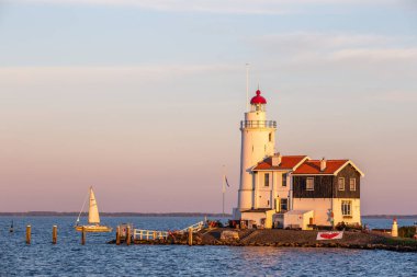 paard van marken lighthouse on marken island in golden hour with blue sky and sea with sailing boat