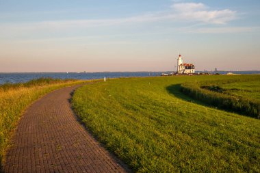 stone path guiding towards paard van marken lighthouse on marken island in golden hour
