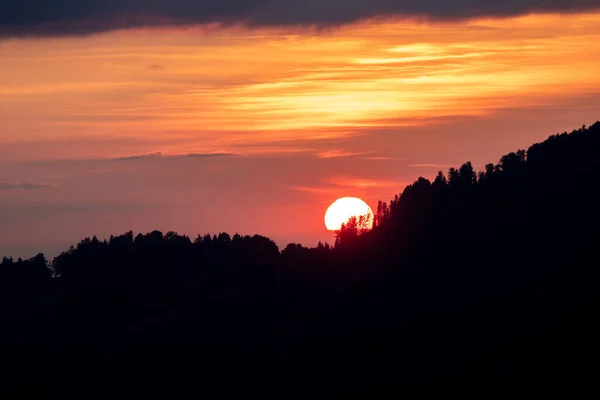 sunset with sun over forest silhouette and glowing cloudy sky
