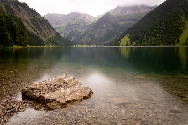 rock in mountain lake with crystal clear water, smooth surface and slightly blurred background in austrian alps vilsalpsee