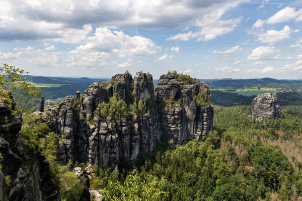 Majestic rock formations rise high above dense green forests under a vibrant sky at Schrammsteine in Saxon Switzerland, showcasing natural beauty in the Elbe Sandstone Mountains.