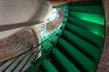 Çelikten yapılmış sarmal yeşil merdiven. Görünür tuğlalardan yapılmış eski binanın içi.