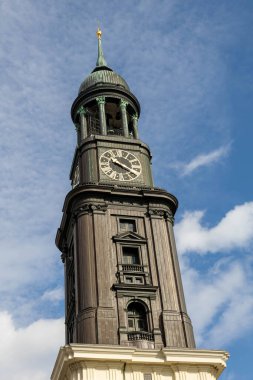 Hamburg, Almanya 'da etkileyici mimari tasarımını sergileyen grevci bir kilise kulesi yükseliyor. Yapı, parlak mavi gökyüzüne karşı belirgin bir saat yüzüne sahip..