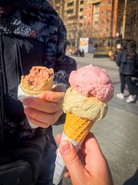 Güneşli bir günde açık havada yapılan renkli zanaatkar dondurma külahları kremalı çilek, vanilya ve çikolata kepçelerini kalabalık bir şehir arka planına karşı waffle külahlarında gösteriyor..