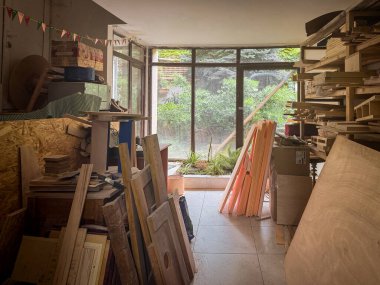 Güneşli marangozluk stüdyosu, kereste yığınları, büyük pencereler ve ahşap işçiliği için düzgün düzenlenmiş çiğ tahtalar, parlak, ışık dolu bir iç mekan..