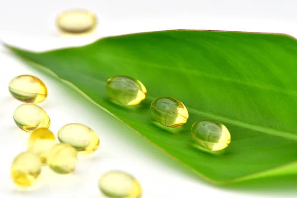 Wellness with natural product concept with oil capsule and green leaf on white background.