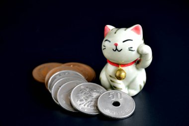 Maneki-neko 'nun küçük el yapımı çömleği, şanslı kedi ve Japon parası karanlık arka planda..