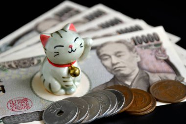 Maneki-neko 'nun küçük el yapımı çömleği, şanslı kedi ve Japon parası karanlık arka planda..