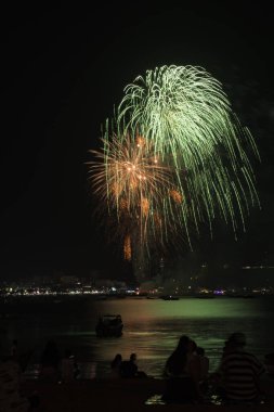 İnsanlarla dolu renkli havai fişekler ve deniz kenarındaki gece lambaları kutlamaları..