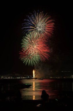 İnsanlarla dolu renkli havai fişekler ve deniz kenarındaki gece lambaları kutlamaları..