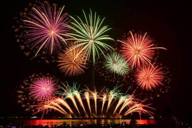 İnsanlar cep telefonlarıyla havai fişek gösterisi çekiyor. Renkli havai fişek kutlamaları ve plajda kalabalık insanlarla dolu gökyüzü arka planı..