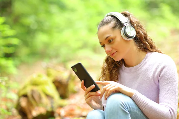 ヘッドフォンを装着したリラックスした女性が森の中で音楽や携帯電話のコンテンツを聞いて — ストック写真