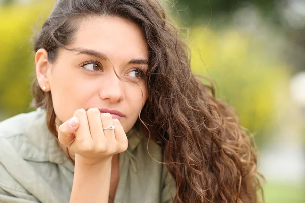 Serious woman with engagement ring looks away in a park
