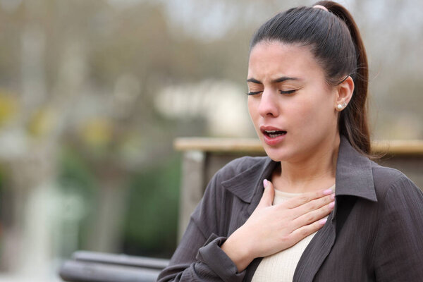 Woman with breathing problems sitting and complaining in a park