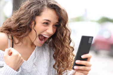 Excited woman celebrating checking phone in the street