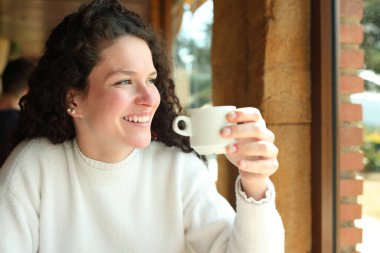 Happy woman drinking coffee looking away in a restaurant
