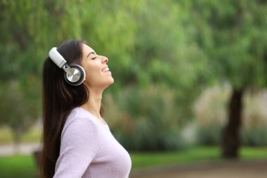 Side view portrait of a happy woman breathing listening audio guide in a park