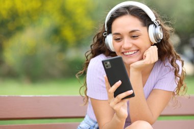 Happy woman sitting in a bench in a park using listening to music