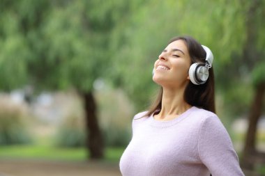 Happy woman breathing fresh air with headphones on green background in a park